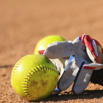 A softball glove and softballs on a softball diamond.