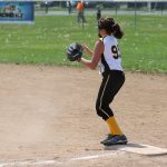 A girl playing softball at first base with a runner approaching