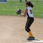 A first base softball player blocking the base from a runner